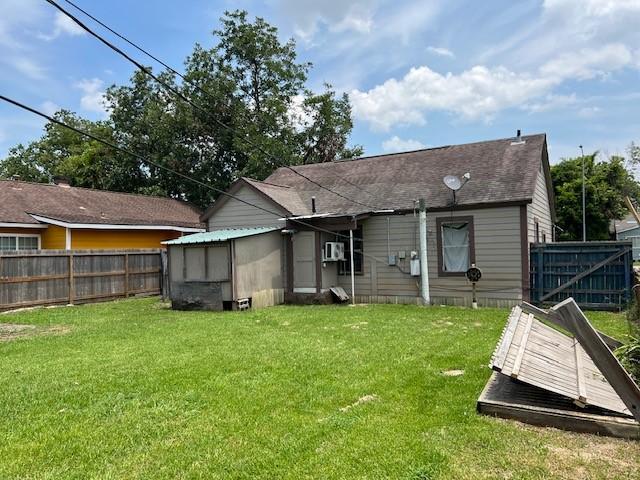 back of house with a lawn, a shingled roof, and fence