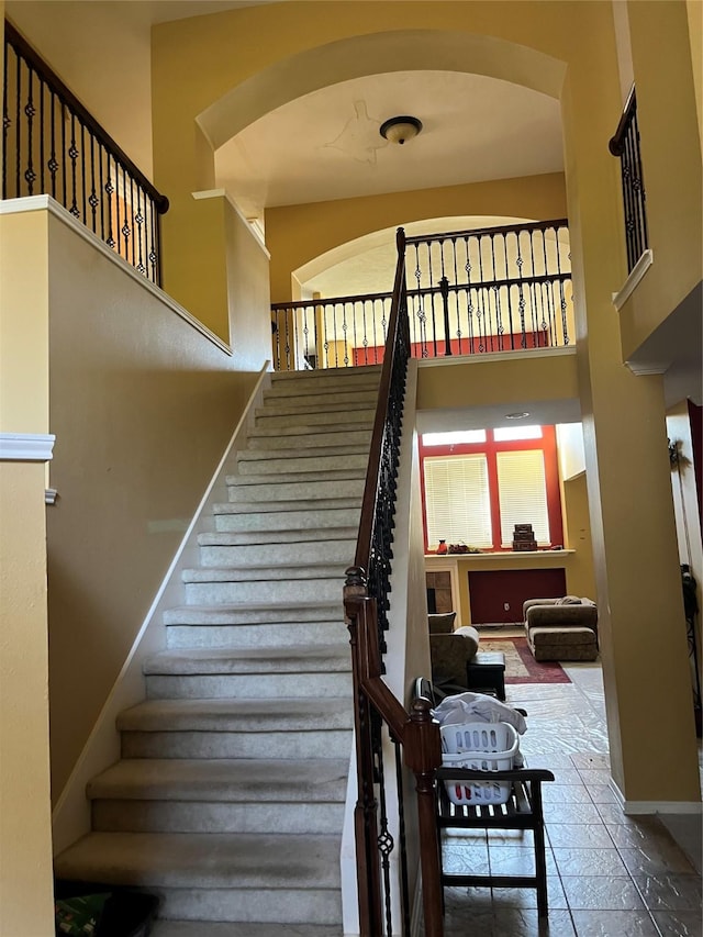 stairway featuring baseboards, arched walkways, and a towering ceiling