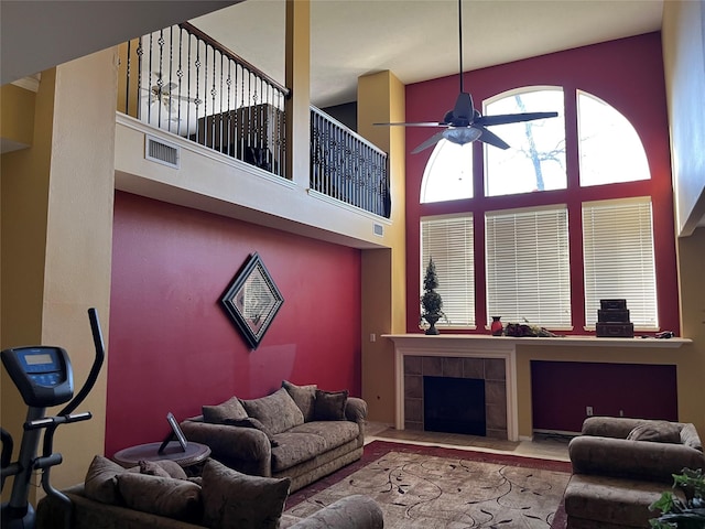 living area featuring a ceiling fan, a high ceiling, a fireplace, and visible vents