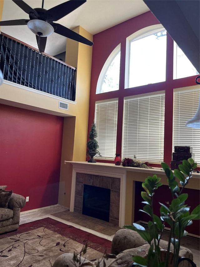 living area featuring wood finished floors, visible vents, a high ceiling, ceiling fan, and a tile fireplace