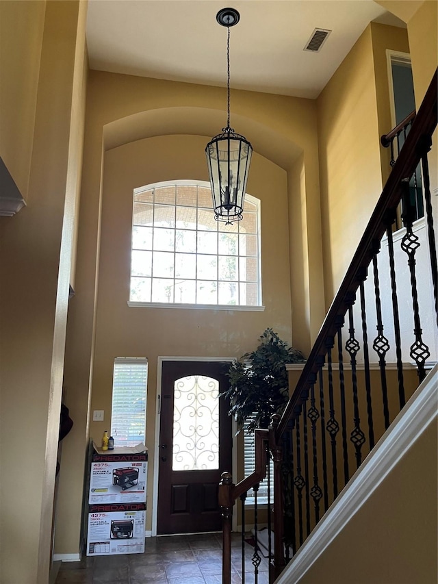 entrance foyer with stairway, visible vents, a towering ceiling, and a chandelier