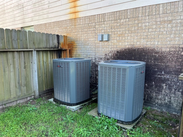 details featuring cooling unit, fence, and brick siding