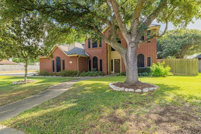 view of front of house with brick siding, a shingled roof, a front yard, and fence