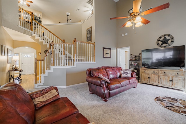 carpeted living room featuring visible vents, a ceiling fan, stairway, a high ceiling, and baseboards