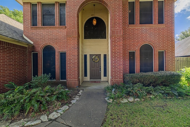 view of exterior entry featuring brick siding and roof with shingles