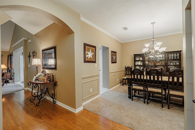 dining room featuring visible vents, arched walkways, light wood-style floors, an inviting chandelier, and a decorative wall