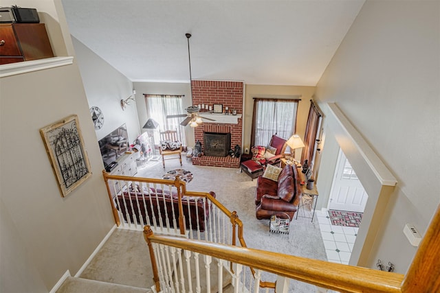 living area featuring stairway, carpet flooring, baseboards, a brick fireplace, and ceiling fan