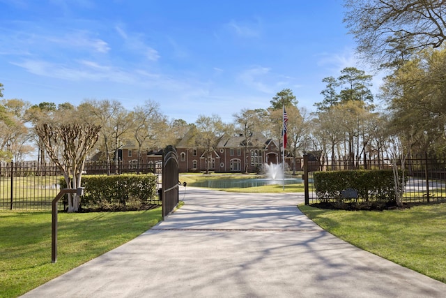 view of property's community with a lawn, concrete driveway, and fence