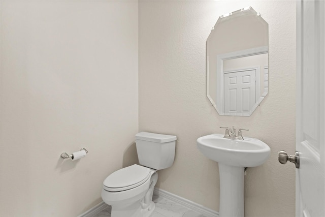 half bathroom featuring a sink, baseboards, toilet, and marble finish floor