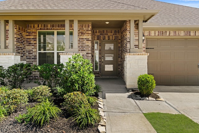 doorway to property featuring covered porch, brick siding, a garage, and a shingled roof