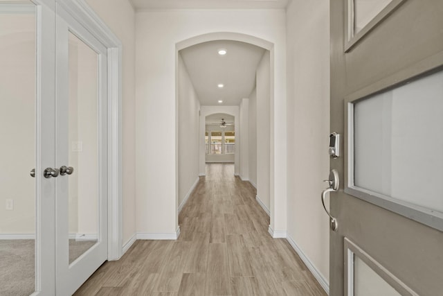 corridor with recessed lighting, baseboards, arched walkways, and light wood finished floors