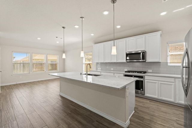 kitchen with tasteful backsplash, dark wood-type flooring, a center island with sink, appliances with stainless steel finishes, and a sink