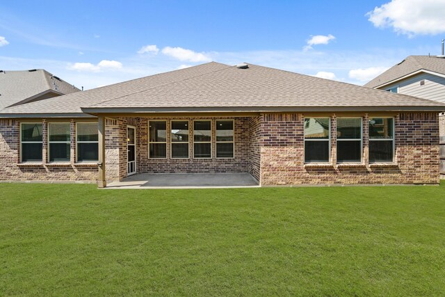 rear view of house featuring brick siding, a patio area, a lawn, and a shingled roof