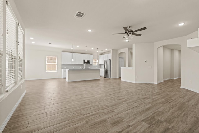 unfurnished living room with a ceiling fan, arched walkways, visible vents, and light wood finished floors