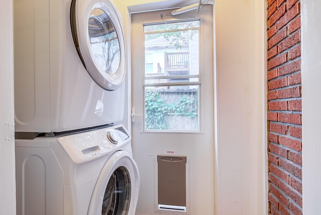 washroom with stacked washer / dryer, brick wall, and laundry area