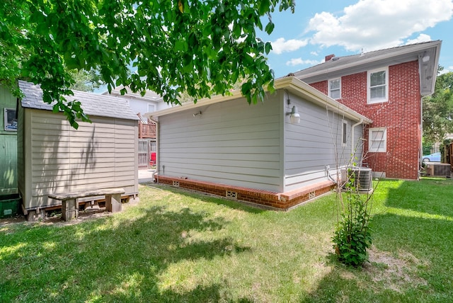 back of house featuring a storage unit, central air condition unit, an outbuilding, and a lawn