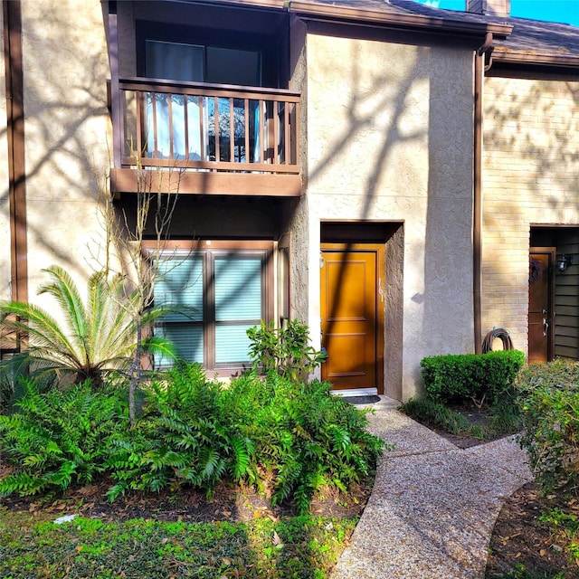 entrance to property with a balcony, brick siding, and stucco siding