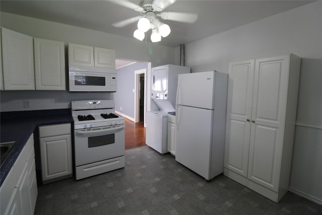 kitchen featuring stacked washer and dryer, a ceiling fan, dark countertops, white cabinetry, and white appliances