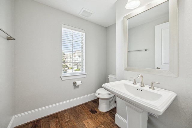 half bathroom featuring wood finished floors, visible vents, baseboards, a sink, and toilet