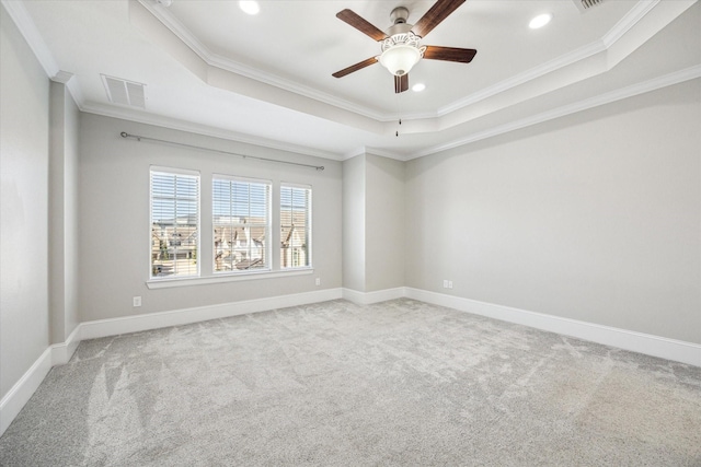 spare room with a tray ceiling, visible vents, carpet floors, and ornamental molding