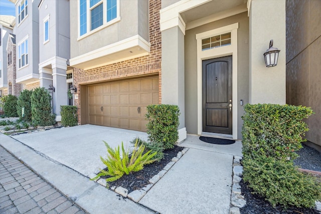 view of exterior entry with concrete driveway, an attached garage, brick siding, and stucco siding