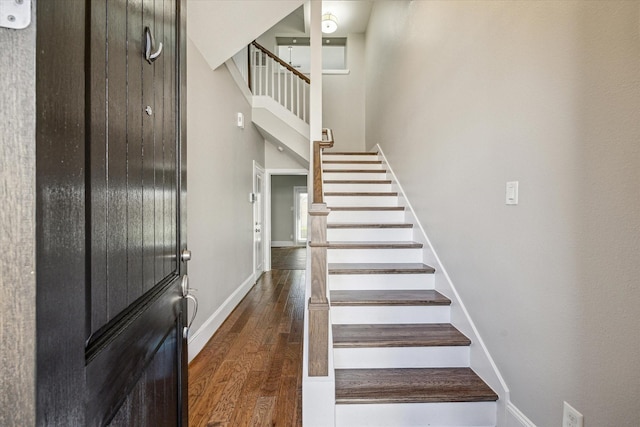 stairs with a high ceiling, wood finished floors, and baseboards