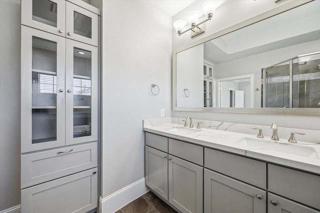 full bath featuring a shower stall, double vanity, baseboards, and a sink