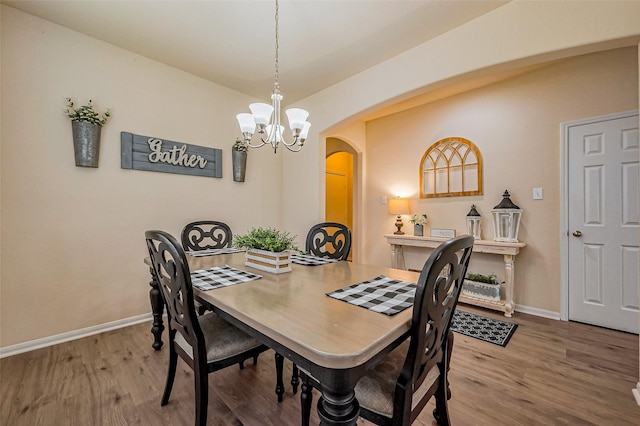 dining area featuring arched walkways, a chandelier, baseboards, and wood finished floors