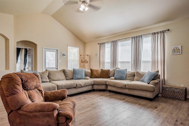 living area featuring arched walkways, light wood-style flooring, high vaulted ceiling, and a ceiling fan