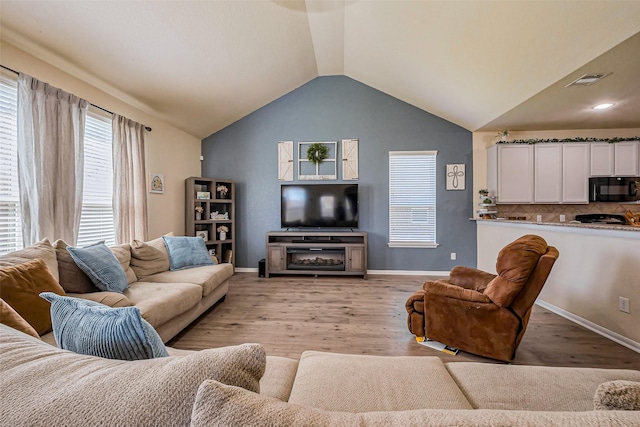 living area with baseboards, light wood-type flooring, lofted ceiling, and visible vents