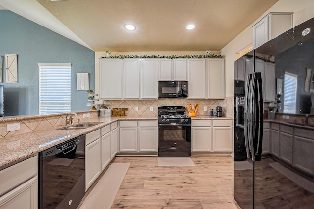 kitchen with light wood-type flooring, a sink, black appliances, vaulted ceiling, and tasteful backsplash