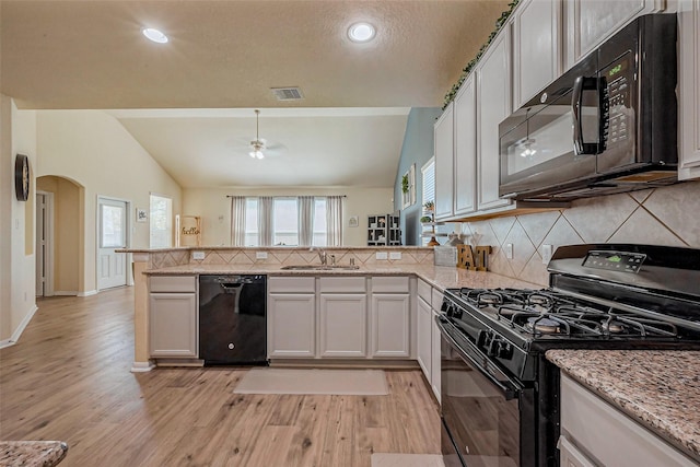 kitchen featuring visible vents, black appliances, a sink, arched walkways, and a peninsula