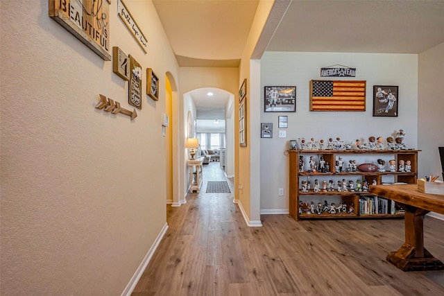 hallway with wood finished floors, arched walkways, and baseboards