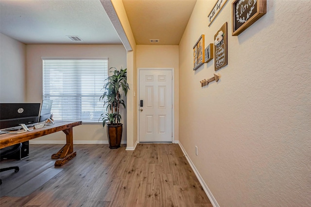 office featuring a textured wall, visible vents, baseboards, and wood finished floors