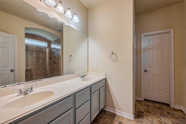 full bath featuring double vanity, tiled shower, baseboards, and a sink