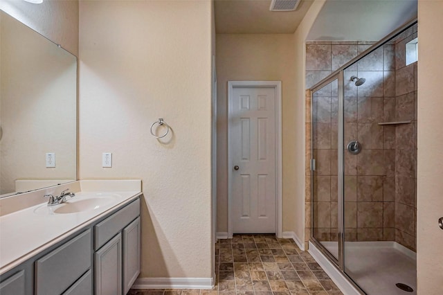 bathroom featuring visible vents, a shower stall, stone finish flooring, baseboards, and vanity