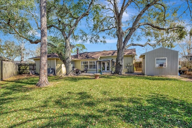 back of house featuring a shed, french doors, a yard, a fenced backyard, and an outbuilding