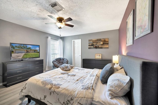 bedroom with light wood-type flooring, visible vents, a textured ceiling, and a ceiling fan