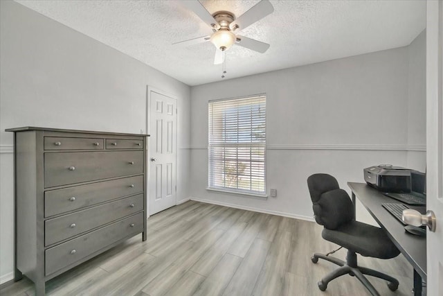 office area with ceiling fan, baseboards, light wood finished floors, and a textured ceiling