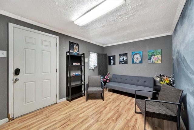 sitting room with baseboards, light wood-style flooring, a textured ceiling, crown molding, and a textured wall