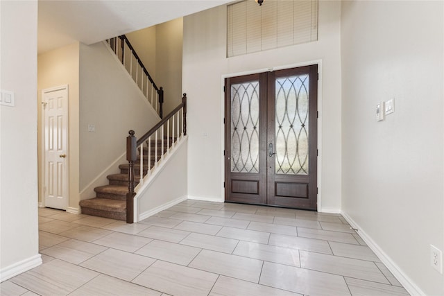 foyer entrance featuring french doors, baseboards, a high ceiling, and stairs