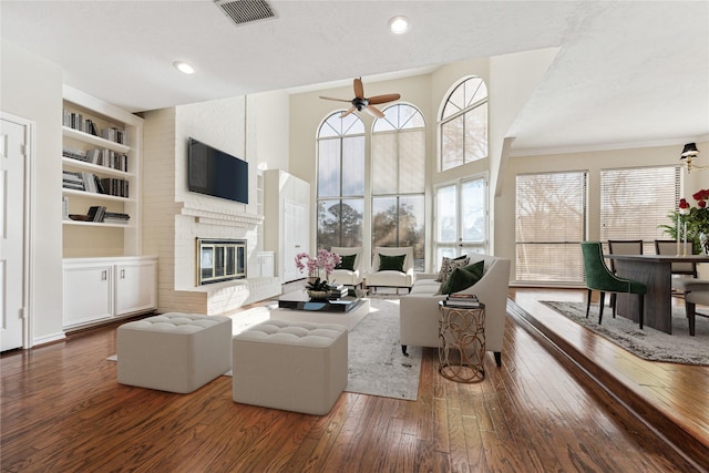 living area with visible vents, a ceiling fan, hardwood / wood-style flooring, built in features, and a fireplace