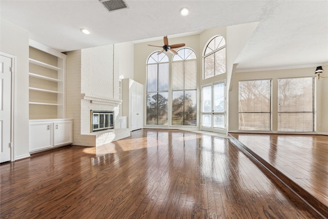 unfurnished living room featuring built in features, visible vents, a fireplace, ceiling fan, and wood-type flooring