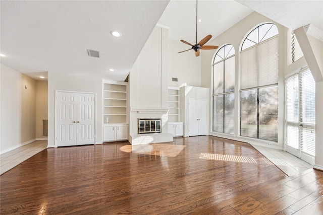 unfurnished living room featuring visible vents, a ceiling fan, built in features, wood finished floors, and a fireplace