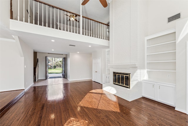 unfurnished living room featuring visible vents, built in shelves, wood finished floors, a fireplace, and baseboards