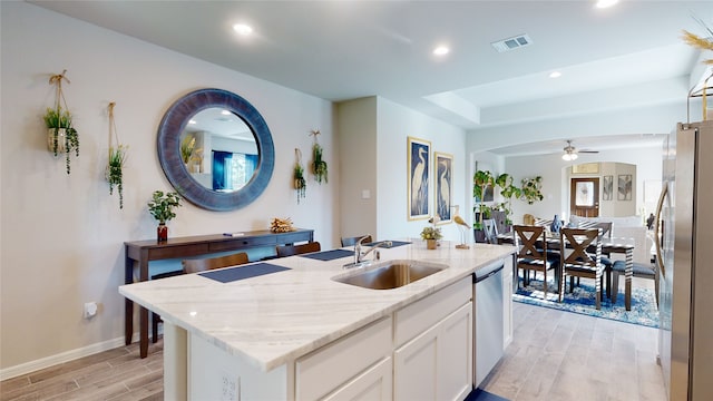 kitchen featuring visible vents, wood tiled floor, stainless steel appliances, a sink, and white cabinetry