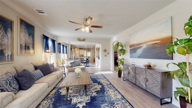 living area with baseboards, wood finished floors, visible vents, and ceiling fan