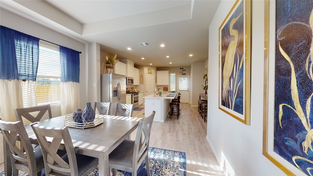 dining room featuring light wood-type flooring, visible vents, plenty of natural light, and a tray ceiling