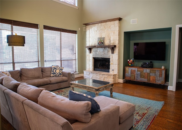 living area with a stone fireplace, a high ceiling, wood finished floors, and baseboards