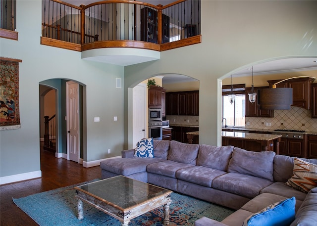 living area with arched walkways, a towering ceiling, baseboards, and dark wood-style flooring